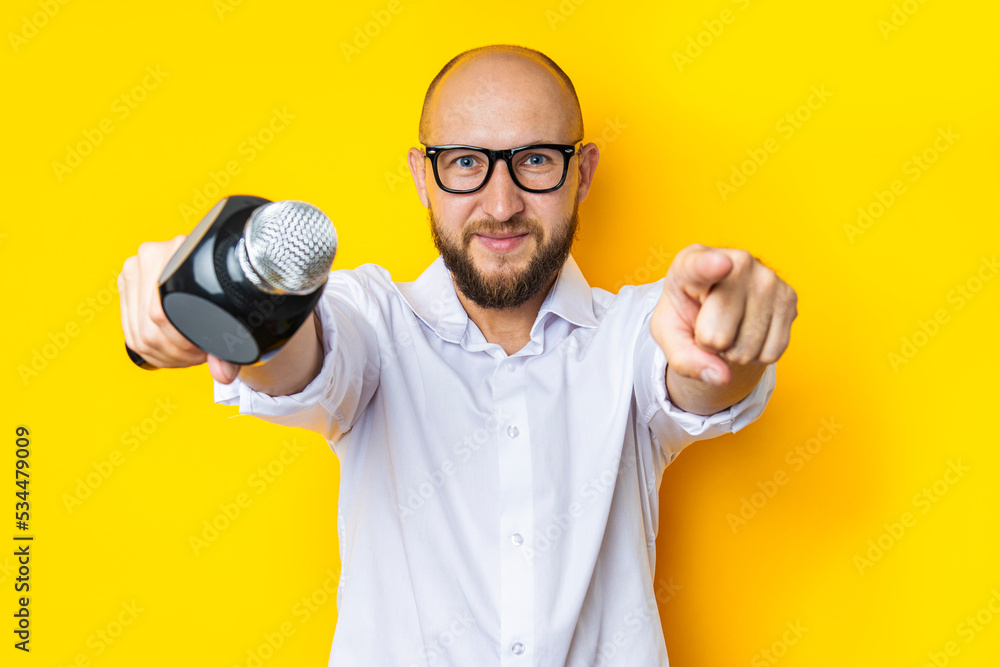 Singing young man with a microphone points in front of him on a yellow background Singing young man with a microphone points in front of him on a yellow background