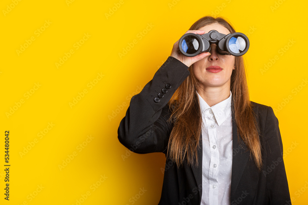 young business woman looking through binoculars on a yellow background young business woman looking through binoculars on a yellow background