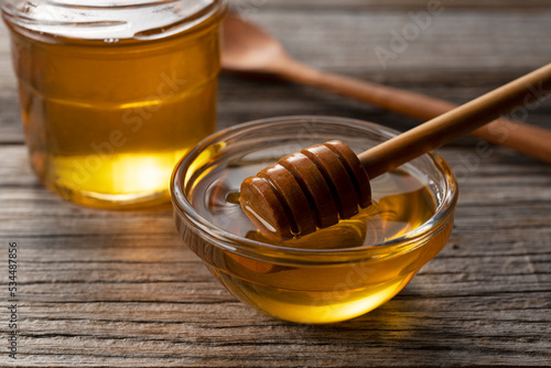 Cuadro en lienzo Honey and wooden honey dipper in glass container on old wooden background