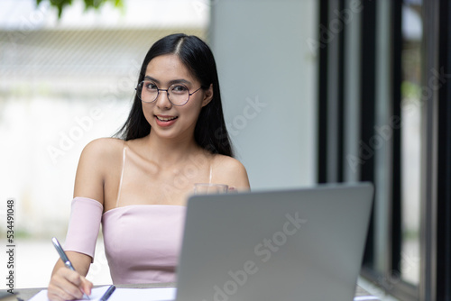 Free Download Charming and good-humored Asian woman is working on a laptop in the backyard. Working from home. - GFXLoad