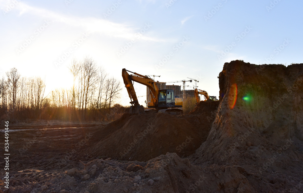 Excavator on earthmoving on sunset background. Loader on excavation. Excavator digs gravel. Earth-Moving Heavy Equipment for Construction. Earth mover ar construction site. Backhoe Loader. Excavator on earthmoving on sunset background. Loader on excavation. Excavator digs gravel. Earth-Moving Heavy Equipment for Construction. Earth mover ar construction site. Backhoe Loader.