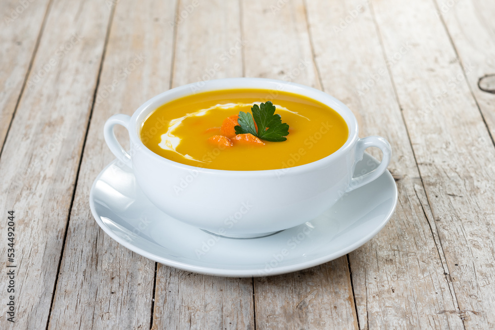 Carrot soup with cream and parsley on rustic wooden table Carrot soup with cream and parsley on rustic wooden table