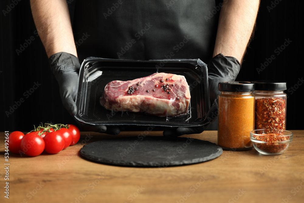 The chef is holding a beef steak in a store's plastic packaging.