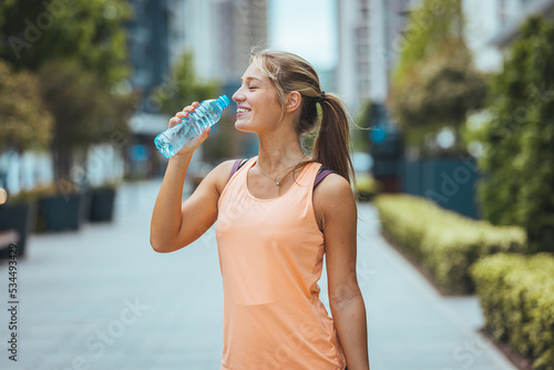 Cropped shot of a young woman enjoying a bottle of water while out for a run. Portrait Of Beautiful Athletic Girl In Bright Colorful Sportswear Resting After Fitness Workout.