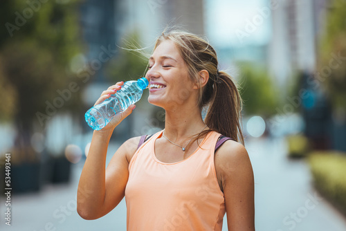 Close up portrait of a young long-haired stylish female drinking water with her eyes closed outdoors. Healthy woman drinking water after exercising. Fitness woman taking a break after workout.