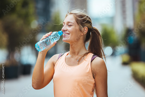 Fitness thirsty girl drinking water. Portrait of sweaty woman take a break after intense workout. Mid adult fit woman taking a break and drink from water bottle after gym workout