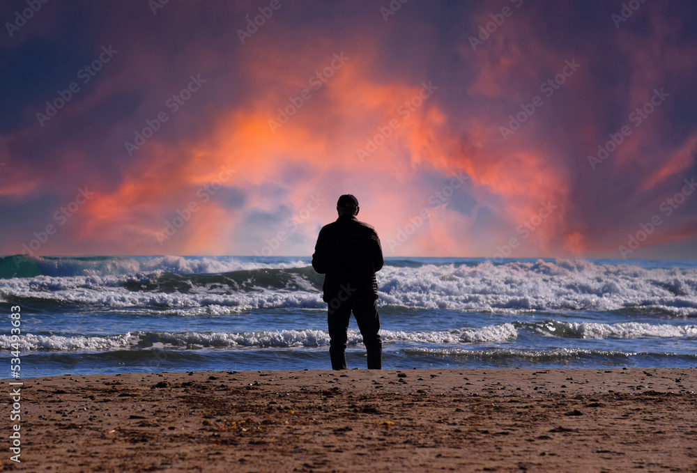 Man at sea. Back side of European man 40-70s in black jacket, standing and waiting or thinking about something, in feeling lonely sadness. Male silhouette at the beach sea on blue sky background.