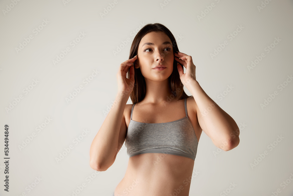Portrait of young tender woman posing in cotton top isolated over grey studio background. Female cosmetology treatment Portrait of young tender woman posing in cotton top isolated over grey studio background. Female cosmetology treatment