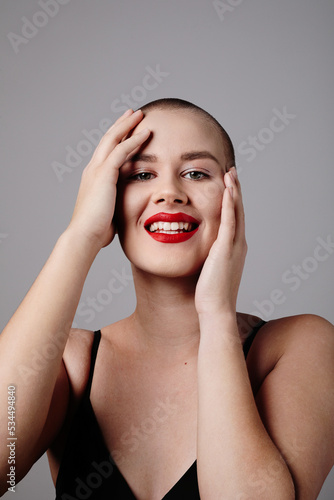 Smiling young bald woman posing over light grey background. Vertical mock-up.