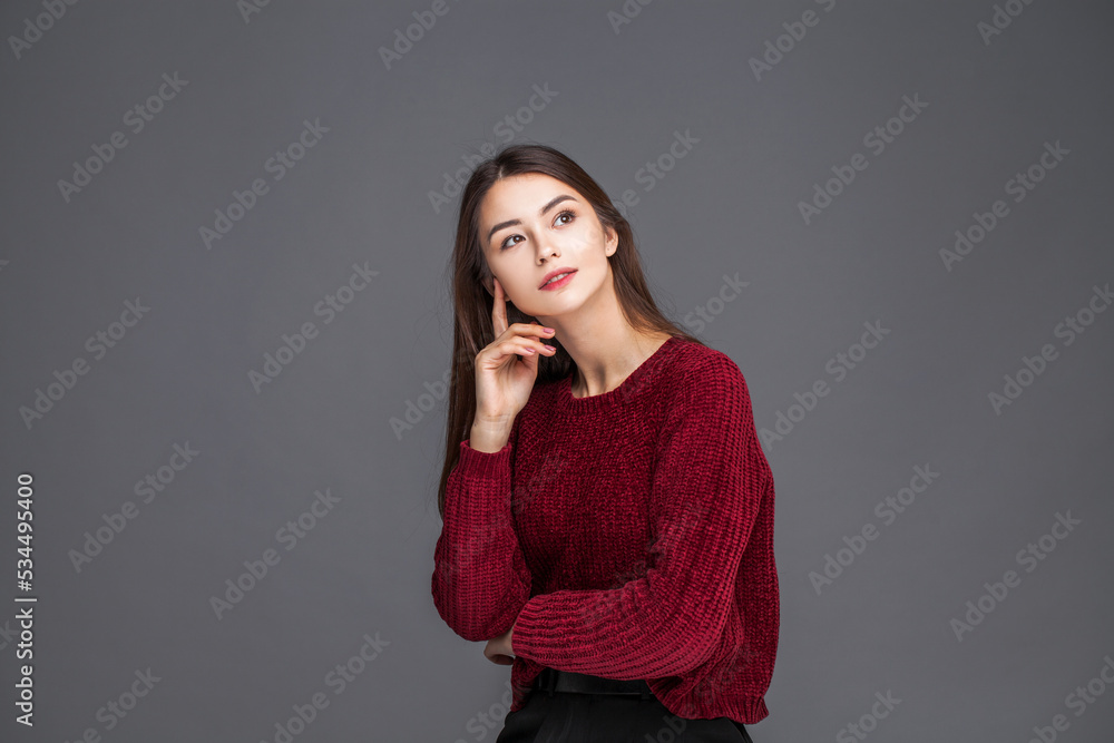 Young beautiful girl in a knitted red sweater posing isolated on grey background Young beautiful girl in a knitted red sweater posing isolated on grey background
