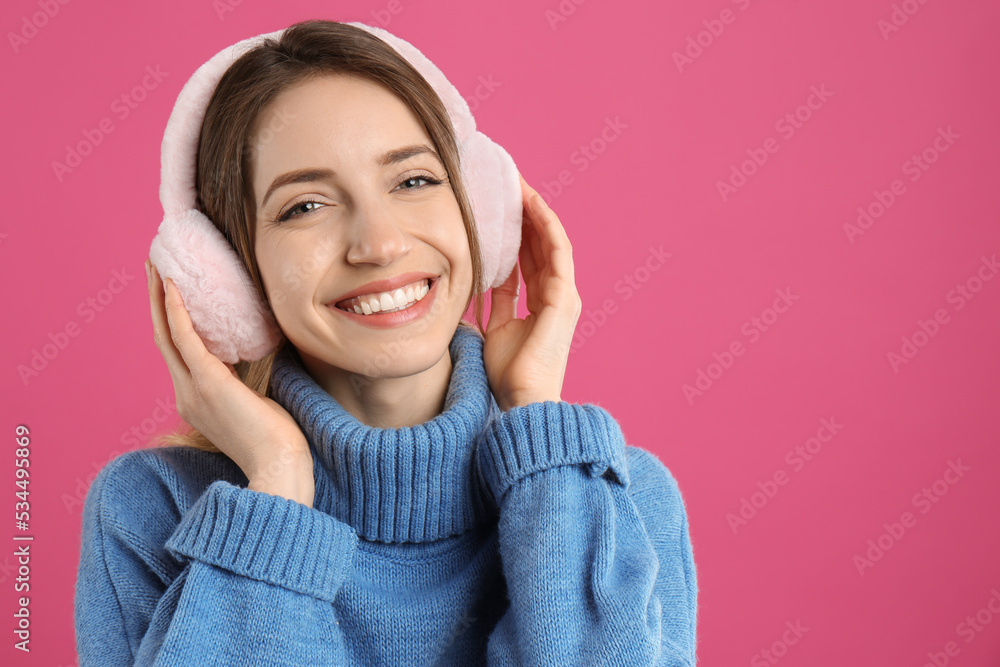 Happy woman wearing warm earmuffs on pink background, space for text Happy woman wearing warm earmuffs on pink background, space for text
