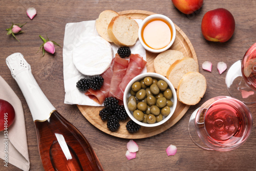 Delicious rose wine and snacks on wooden table, flat lay