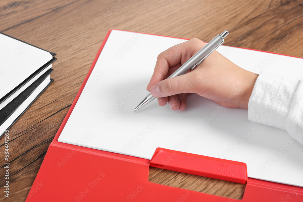 Woman writing on sheet of paper in red folder at wooden table, closeup Woman writing on sheet of paper in red folder at wooden table, closeup