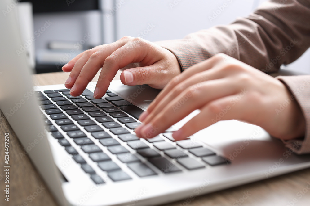 Woman working on laptop at wooden table in office, closeup Woman working on laptop at wooden table in office, closeup