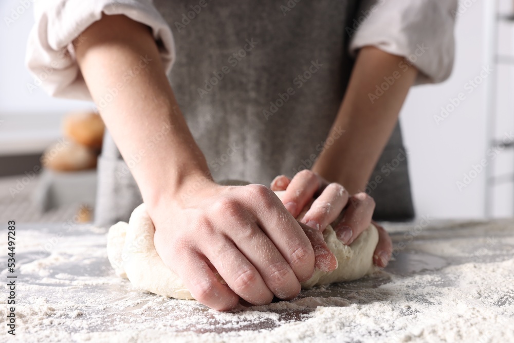 Woman kneading dough at table in kitchen, closeup