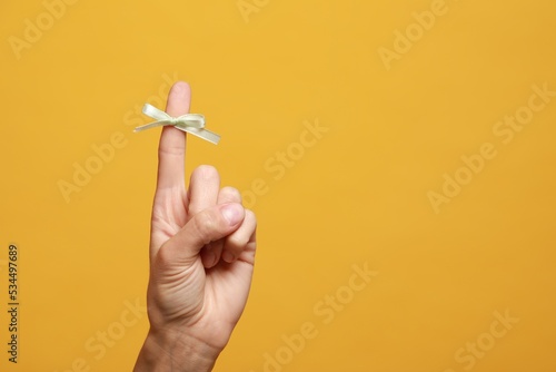 Woman showing index finger with tied bow as reminder on orange background, closeup. Space for text photo