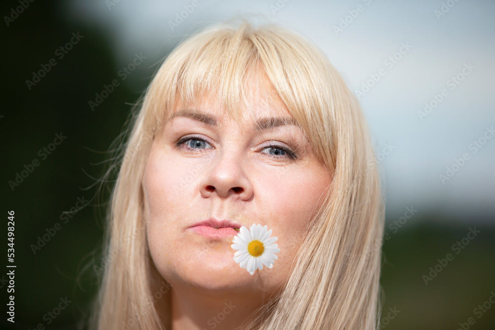 A middle-aged woman with white hair holds a chamomile flower in her mouth. A middle-aged woman with white hair holds a chamomile flower in her mouth.