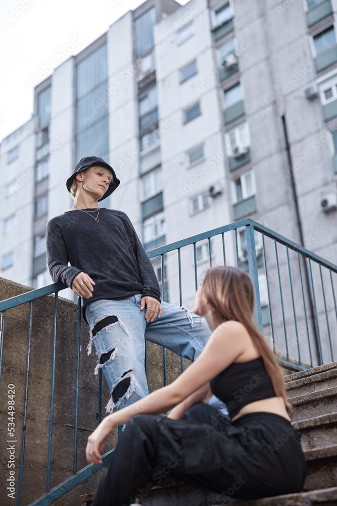 Teenagers hang out in the urban exterior on the stairs surrounded by the buildings.