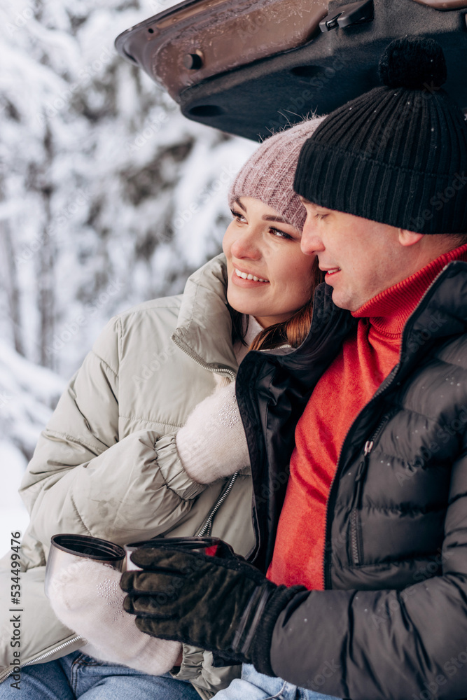 Young couple in love sitting in an embrace in the open trunk of a car,drinking tea in a winter forest.Winter activities,active lifestyle,Valentine's day,tenderness and love. Young couple in love sitting in an embrace in the open trunk of a car,drinking tea in a winter forest.Winter activities,active lifestyle,Valentine's day,tenderness and love.