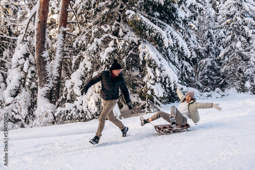 Obraz na plátně Young couple in love is sledding in a winter forest and having fun spending time together