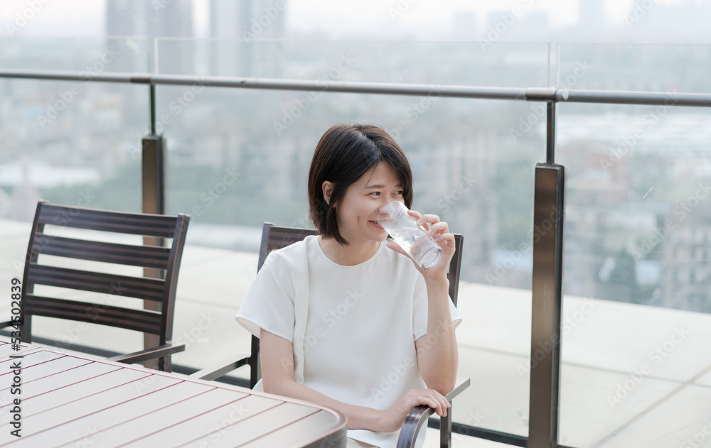 Fototapeta premium Relaxed woman sitting in chair on balcony and holding a glass of water 