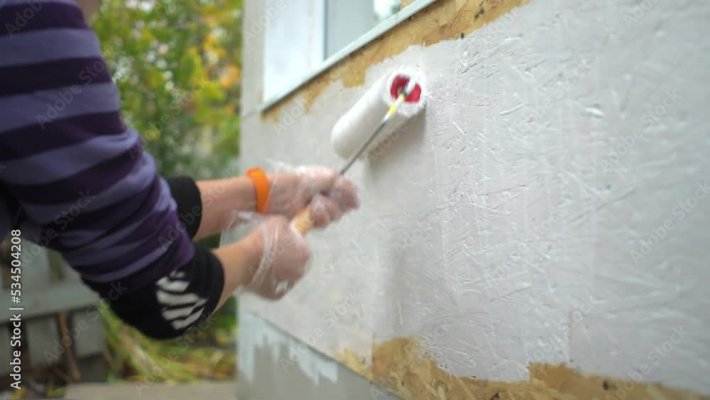 Woman worker paints the wall between windows and base of her own house Woman worker paints the wall between windows and base of her own house