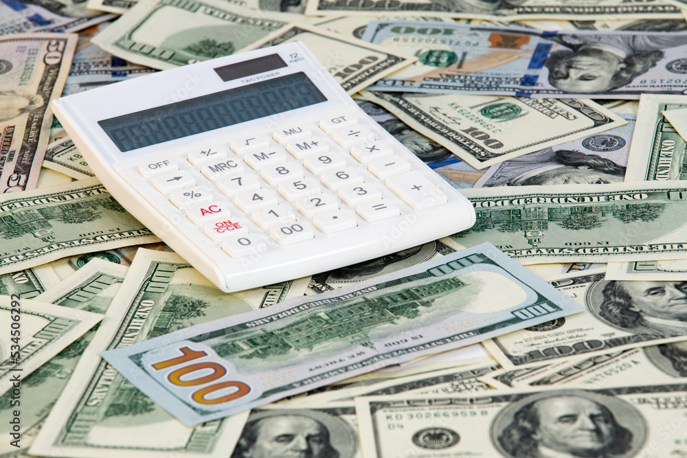A lot of money dollars with white calculator on desk. Exchange or saving concept. Paper banknotes A lot of money dollars with white calculator on desk. Exchange or saving concept. Paper banknotes