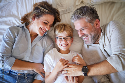 Foto Family, tickling and child lying on bed with his happy mom and dad laughing and having fun in their bedroom at home