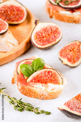 Bruschetta with raw ripe fig, cream cheese, prosciutto, walnuts and herbs on white table. Healthy quick breakfast idea. Italian cuisine. Selective focus, vertical image