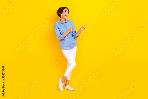 Full length photo of good mood excited girl dressed blue looking pointing two fingers empty space isolated yellow color background © deagreez