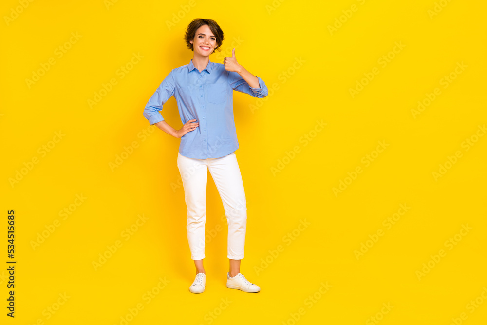 Full length photo of cute confident girl dressed blue shirt showing thumb up empty space isolated yellow color background Full length photo of cute confident girl dressed blue shirt showing thumb up empty space isolated yellow color background
