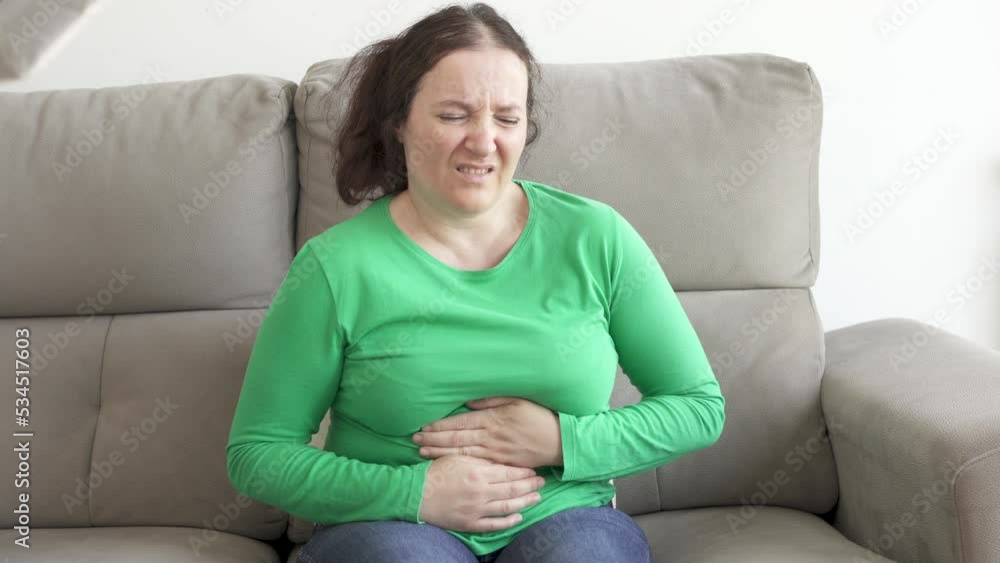 Woman experiencing stomach ache while sitting on sofa at home Woman experiencing stomach ache while sitting on sofa at home