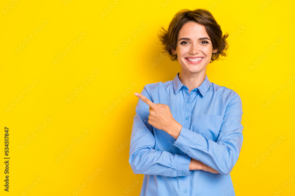 Portrait photo of young confident woman wear blue shirt formal office clothes employer toothy smile finger point empty space isolated on yellow color background
