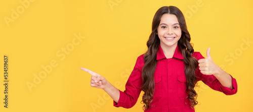 cheerful child girl pointing finger on copy space with thumb up gesture, success. Child face, horizontal poster, teenager girl isolated portrait, banner with copy space.