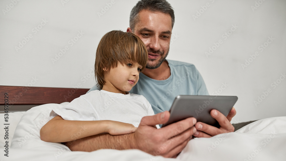 Father and little son watch tablet in bed at home Father and little son watch tablet in bed at home