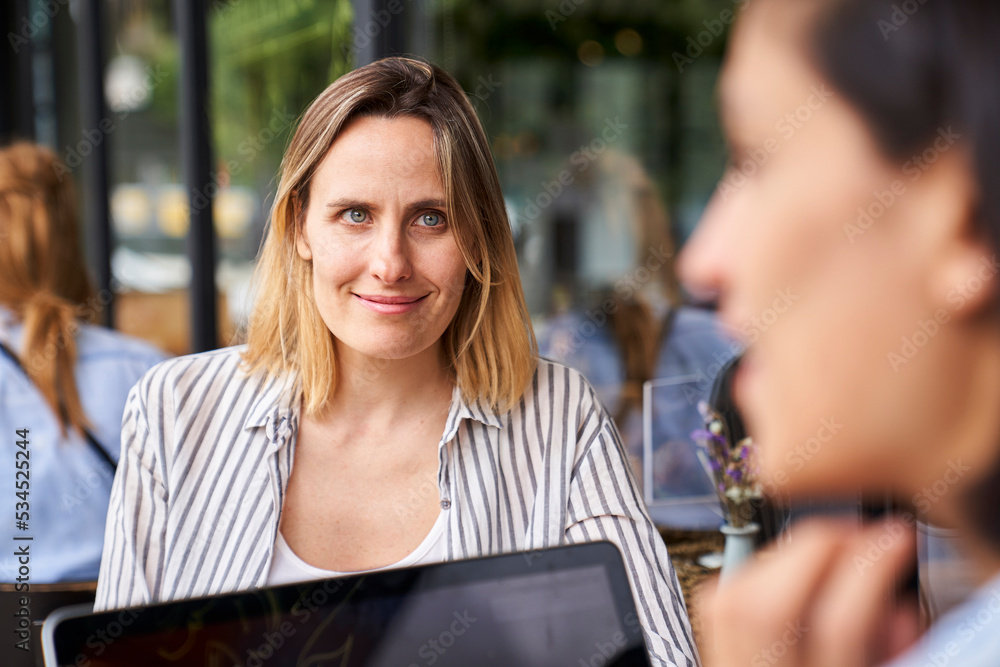 Front view of female entrepreneur working with her Latin-American partner seen out of focus from behind Front view of female entrepreneur working with her Latin-American partner seen out of focus from behind