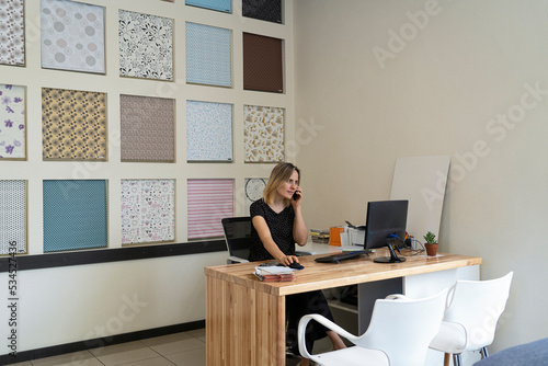 Wide angle view of successful female interior design entrepreneur speaking on phone at her desk