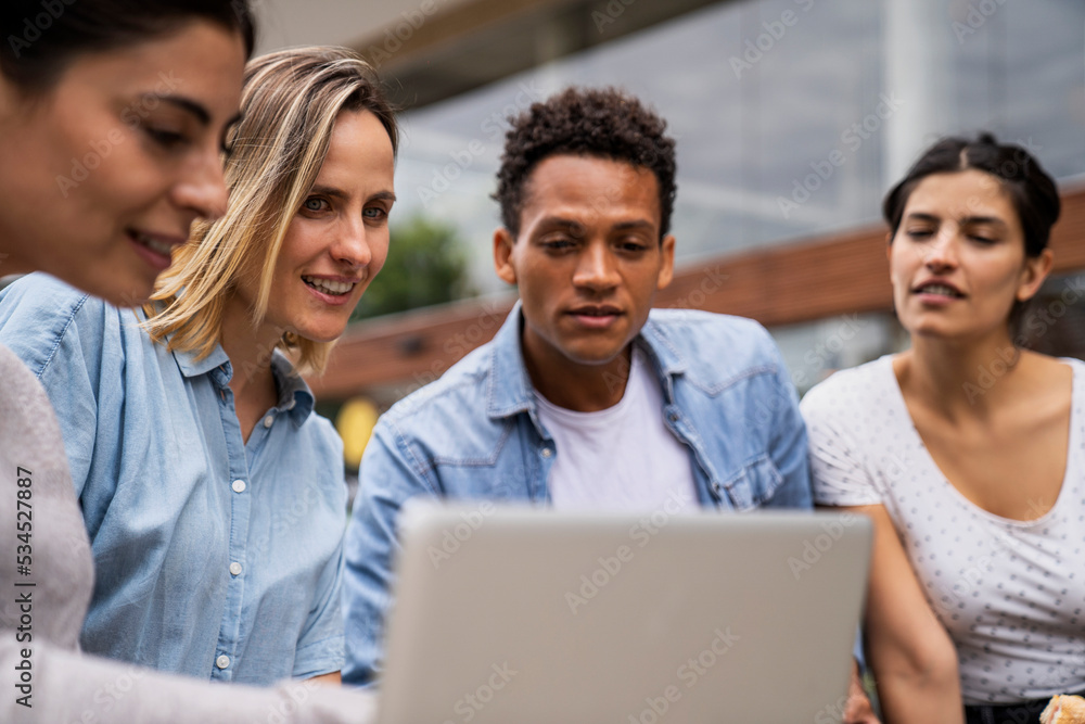 Diverse group of freelance contractor looking at a laptop's screen in an outdoors setting Diverse group of freelance contractor looking at a laptop's screen in an outdoors setting