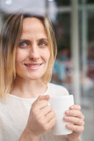 Mid-shot portrait of woman holding a coffee mug while looking through a window