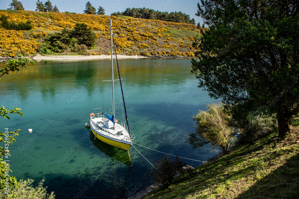 A small wooden sailboat moored on flat calm water in a cove A small wooden sailboat moored on flat calm water in a cove