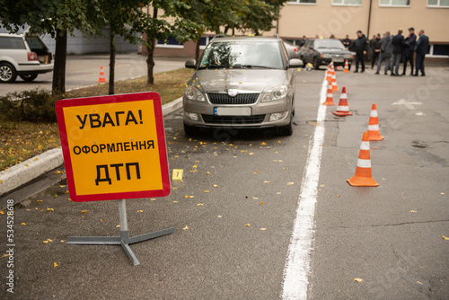 the scene of a traffic accident with car wreckage and police numbers indicating the braking distance and placement of objects, and a sign with the inscription with the text in Ukrainian "Attention reg