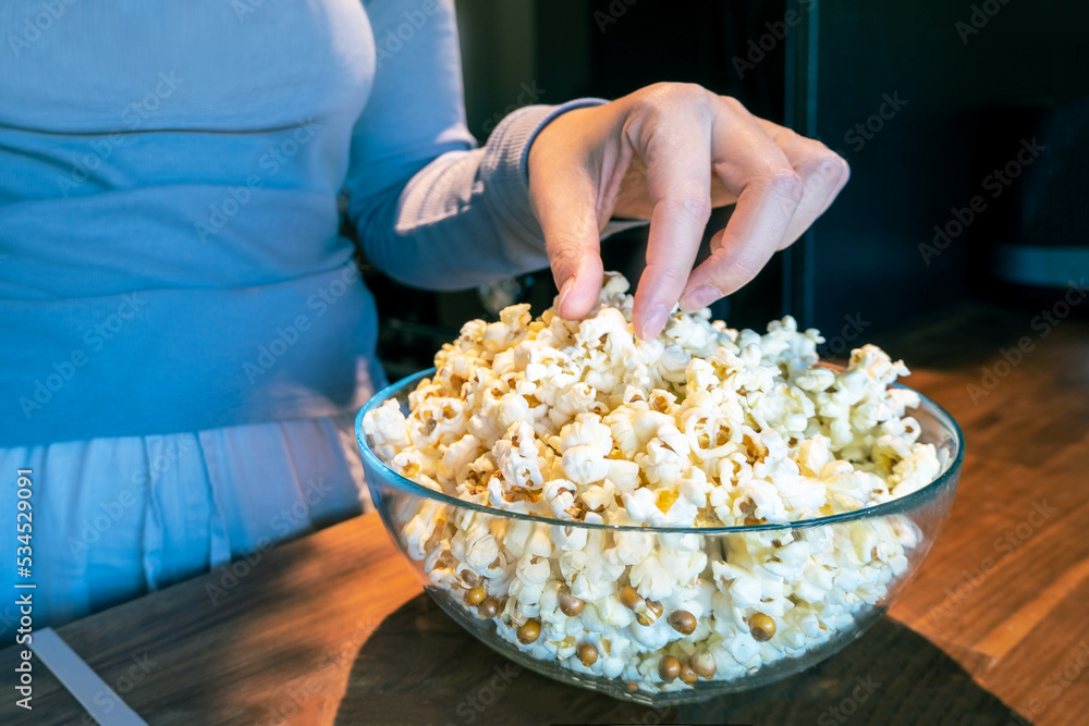Girl reaches for the popcorn in a glass cup in the kitchen. Getting ready to watch a movie Girl reaches for the popcorn in a glass cup in the kitchen. Getting ready to watch a movie