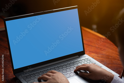 A women hands are typing keyboard playing laptop with blue empty screen on the table, graphic orange light, technology and internet connection concept. copy space for individual text and design