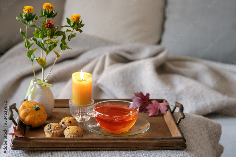 Hot tea and cookies on a tray with candle, flowers and autumn decoration for a relaxing break on the cozy sofa in natural colors, copy space, selected focus