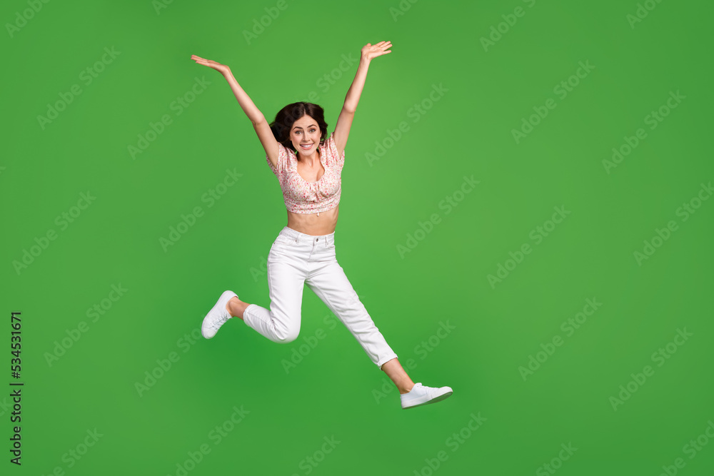 Full length photo of impressed cute girl dressed print blouse jumping high empty space isolated green color background