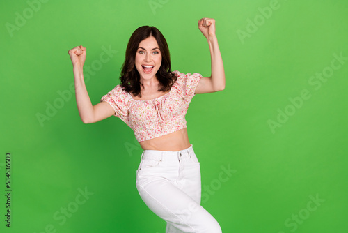 Photo of cute lovely cheerful nice girl with wavy hairstyle dressed blouse hold fists up yell yeah isolated on green color background