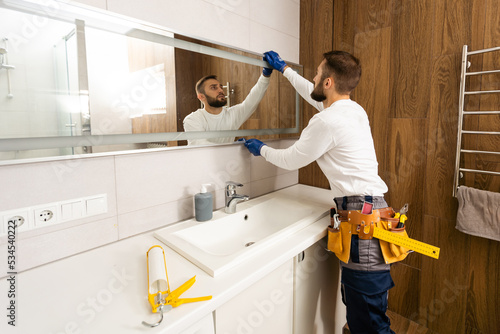 Billede på lærred The worker installs the mirror in the bathroom.
