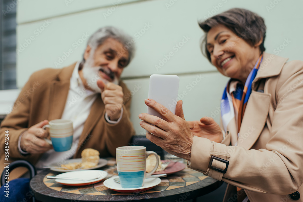 happy senior woman holding smartphone while having brunch with husband on terrace of cafe. happy senior woman holding smartphone while having brunch with husband on terrace of cafe.