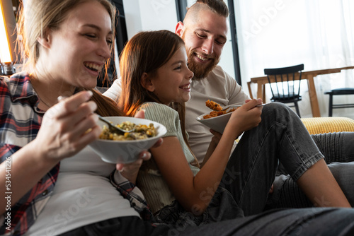 Young modern parents are sitting in the living room with their daughter and eating healthy breakfast. 