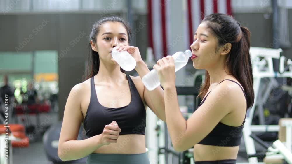 Asian woman doing fitness exercises in the gym taking a break to drink water. Asian woman doing fitness exercises in the gym taking a break to drink water.